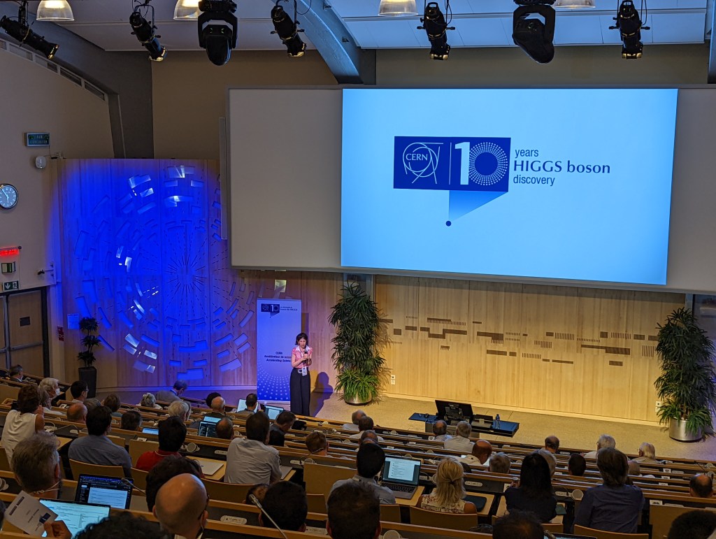 A photo from the CERN auditorium. At the front is CERN's Director General, Dr Fabiola Gianotti and the screen shows the CERN logo with a 10 next to it and the words: "10 years HIGGS BOSON discovery".